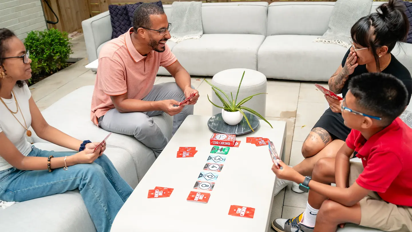 A family laughing over a game of Star Catcher on a backyard patio